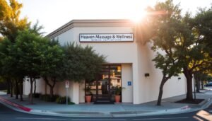 A serene and inviting exterior of the Heaven Massage & Wellness center in Burbank, California. The building is nestled on a tree-lined street, with a welcoming entrance adorned with lush greenery. The warm afternoon sunlight casts a soft glow on the facade, creating a tranquil and inviting atmosphere. The scene captures the convenient location of this haven for relaxation, where visitors can unwind and rejuvenate their minds and bodies.
